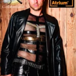 Ein Mann mit kurzen Haaren in Ledermantel, Lederhose und einem Netz-Shirt schaut ernst in die Kamera. Am Nietengürtel trägt er Handschellen